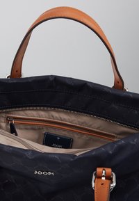 Laulukangaskassi tummansinisenä, jossa on vaalea nahkakahva. Kassissa on vetoketjullinen sisätasku ja vaalea vuori. Logo näkyvissä sisällä.