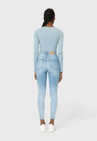 Top de manga larga azul claro combinado con vaqueros de tiro alto azul claro. Textura suave, ajuste delgado y zapatillas blancas completan el look.