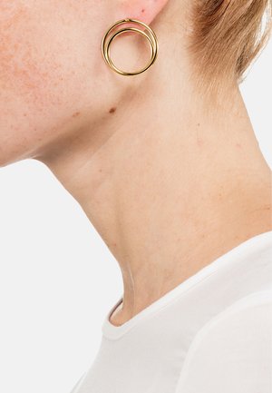 Goldene Creolen mit zwei ineinandergreifenden Kreisen. Glatte, reflektierende Oberfläche mit polierter Oberfläche, vor einem hellen Hintergrund.