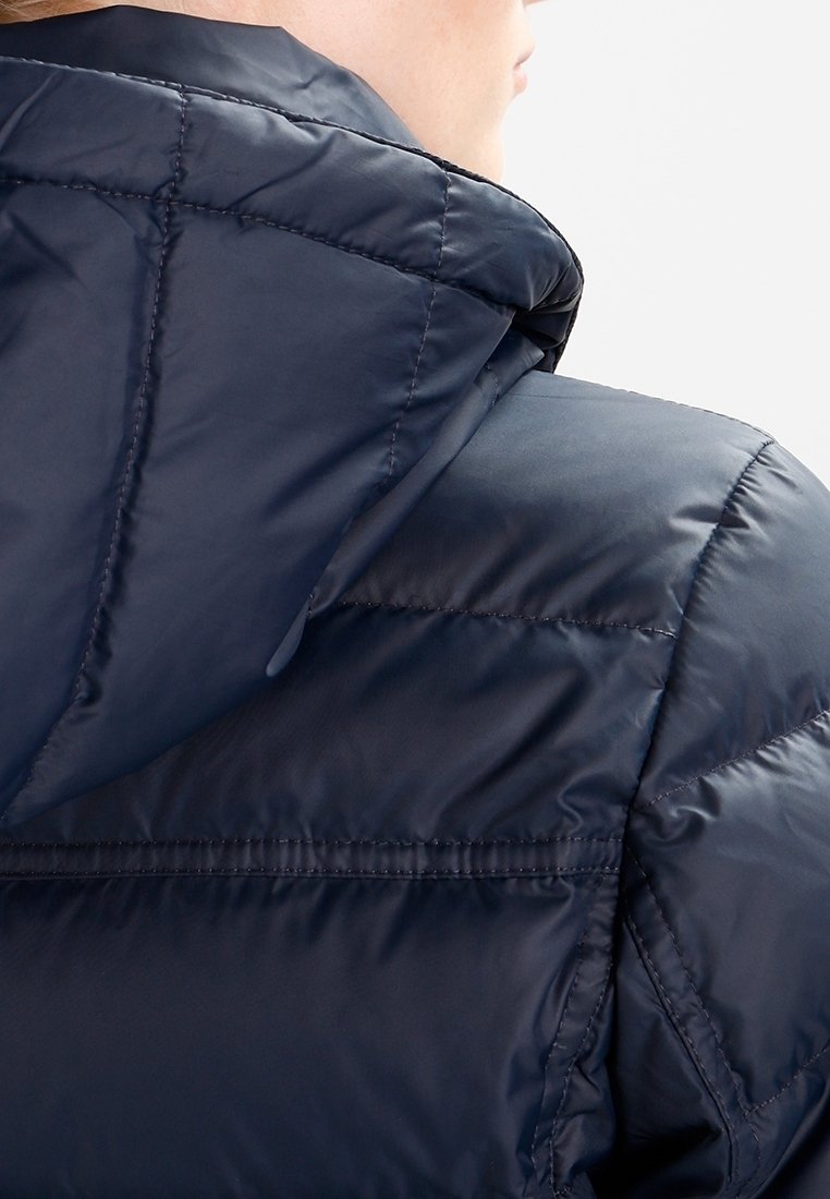 Veste matelassée marine avec un design quilté, un col montant et une capuche. Le matériau semble brillant et lisse avec des détails cousus.