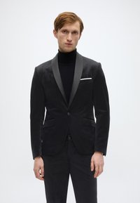 Schwarzer Samtblazer mit Satin-Schalkragen und Ein-Knopf-Verschluss. Verfügt über ein Einstecktuch, zwei Pattentaschen und eine taillierte Passform.