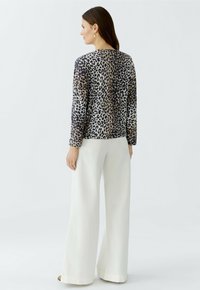Langärmliges Oberteil mit Leopardenmuster in Braun, Schwarz und Beige, kombiniert mit weißen, weit geschnittenen Hosen. Glattes Material, runder Ausschnitt und lässige Passform.
