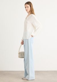 Witte linnen top met een V-hals, gecombineerd met lichtblauwe wijd-pantalon jeans. Beige handtas met een strap en schoenen in neutrale tinten.