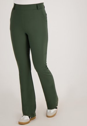 Donkergroene, slim-fit broek van soepel, rekbaar stof met een platte tailleband en details aan de zijkanten. Gecombineerd met lichte schoenen.