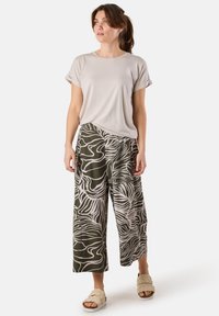 T-shirt beige chiaro con maniche arrotolate, abbinato a pantaloni larghi verde oliva con un motivo astratto ondulato bianco. Sandali casual.