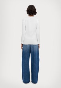 Maglietta bianca a maniche lunghe abbinata a jeans svasati di un blu sbiadito. L'outfit presenta un design pulito con una silhouette semplice e senza motivi visibili.