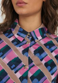 Camicia con colletto in un motivo a righe multicolori che presenta tonalità di rosa, blu, verde e marrone, con una leggera lucentezza e dettagli con bottoni.
