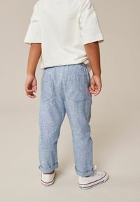 Lysblå, linnedslagsbukser med løs pasform, elastisk talje, to baglommer og opfoldede nederkanter, parret med hvide sneakers.