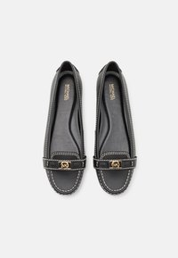 Sorte lær ballet flats med hvit søm og et gullsymbol på frontremmen. Glatt tekstur, rund tå, minimalistisk design.