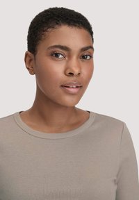 Lichtgrijze, langslavige top met een ronde halslijn, met een gladde textuur en een aansluitend ontwerp, gedragen door een model met kort haar.