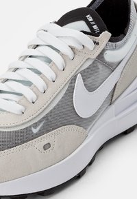 Šviesiai pilki sportbačiai su tinklinio ir zomšinio viršumi, balta „swoosh“ emblema ir baltos raišteliai. Yra paminkštintas padas ir juodas akcentas ant kulno.