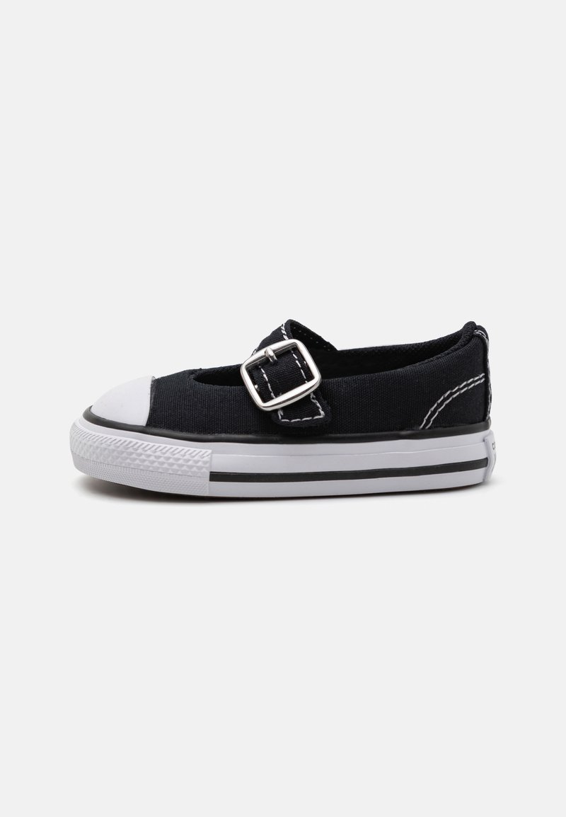 Zapato de lona negro con una puntera de goma blanca, detalle de hebilla plateada y costuras blancas. Presenta un diseño de perfil bajo y rayas en la suela de color negro.