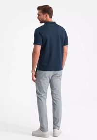 Granatowa koszulka polo z krótkim rękawem, połączona z jasnoszarymi spodniami typu slim-fit. Model w białych trampkach, stoi tyłem do aparatu.