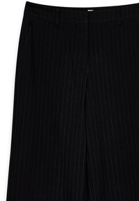 Pantalones negros a medida con finas rayas verticales y sutiles, trabillas para cinturón, detalle de pliegue frontal y bolsillos laterales.