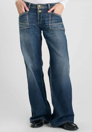 Jeans de mezclilla azul oscuro con un diseño de pierna acampanada, que cuentan con dos bolsillos frontales y costuras de contraste. Los botones en la cintura son de color dorado.