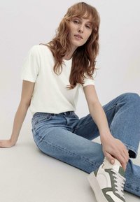 Camiseta blanca de algodón combinada con jeans de mezclilla azul claro. El conjunto incluye zapatillas blancas con acentos verdes y detalles de tela texturizada.