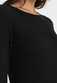 Svart långärmad topp med rund halsringning, mjuk textur, figurnära passform och subtila sömdetaljer längs ärmarna.