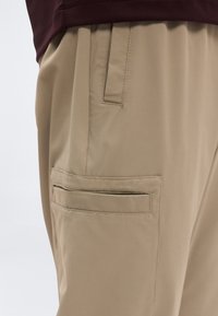 Μπεζ παντελόνι από λείο ύφασμα, με πλαϊνή τσέπη με ραμμένο άκρο και άνετη εφαρμογή. Συνδυασμένο με μπορντό μπλουζάκι.