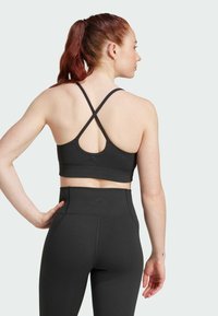 Sujetador deportivo negro con textura acanalada y tirantes cruzados, combinado con leggings de tiro alto, ambos con una mínima marca y una textura suave.