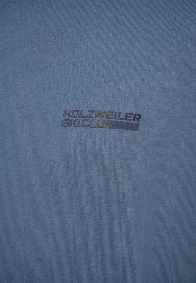 Kék pamut póló, sötétszürke "HOLZWEILER SKICLUB" felirattal, sima textúrával és kerek nyakkivágással.