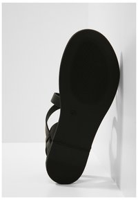 Svarta sandaler med platt sula, tunna remmar och texturerad gummibotten. Klacken har en lätt kurva och en emblemet nära mitten.