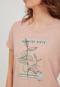 Camiseta de algodón rosa claro con un diseño de impresión botánica en verde y negro, con el texto "PLANTÉS D'ÉTÉ" y detalles del evento a continuación.