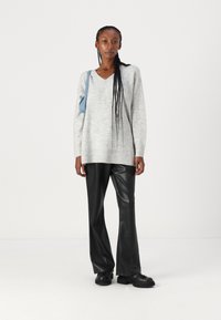 Pull en v gris à manches longues avec des poignets côtelés, associé à un pantalon évasé en simili cuir noir et des chaussures de plateforme noires. Sac bleu clair.