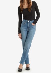 Svart långärmad topp i kombination med ljusblå högmidjade jeans som har framfickor och pryds av små silvernitar. Svarta skor.