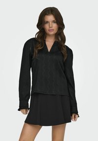 Schwarzes Langarmoberteil mit V-Ausschnitt und subtil strukturiertem Zickzackmuster, kombiniert mit einem schwarzen ausgestellten Rock, beide minimalistisch im Design.