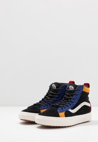 Hoge sneakers met een zwarte suède bovenkant en blauwe, oranje en rode accenten. Witte zijstreep en een textured rubberen buitenzool.