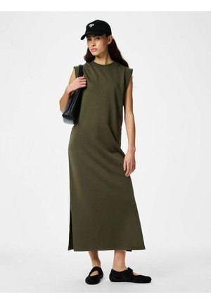 Žena v olivově zelených dlouhých šatech bez rukávů, s černou čepicí, černými balerínami a nesoucí černou kabelku přes rameno.