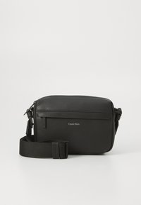 Black leather crossbody bag with textured surface, top zipper, adjustable strap, and embossed Calvin Klein logo on the front.