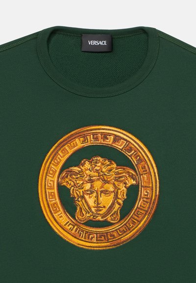 Σκούρο πράσινο πουκάμισο με λεπτομερές χρυσό έμβλημα κεφαλής Μέδουσας στο κέντρο κάτω από το γιακά και μαύρη ετικέτα Versace μέσα στο λαιμό.