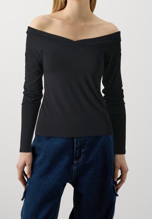 Schwarzes Off-Shoulder-Oberteil mit langen Ärmeln, das mit einem V-Ausschnitt und schmaler Passform ausgestattet ist. Weicher Stoff mit minimaler Textur, kombiniert mit blauen Jeans.