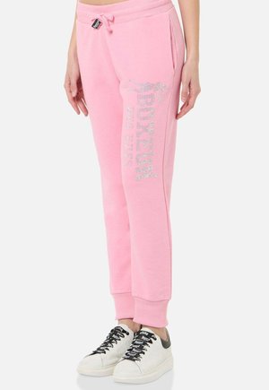 Person, die rosa Trainingshose mit „PAPIER“ Strass-Schrift auf dem Bein und weißen Sneakers mit schwarzen Schnürsenkeln trägt.