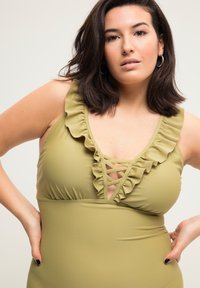 Un maillot de bain une pièce de couleur vert olive avec un ourlet à volants le long de l'encolure et un détail croisées à l'avant. Tissu doux et coupe ajustée.
