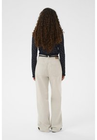 Lys beige brede bukser med baglommer, parret med en mørk langærmet bluse med blomsterprint. Ensfarvet baggrund.