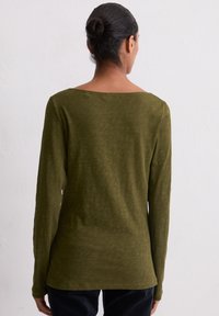 T-shirt z długim rękawem w oliwkowym kolorze, z dekoltem w łódkę i teksturowanym, miękkim materiałem. Szwy boczne wychodzą na dole, co zapewnia luźniejszy krój.