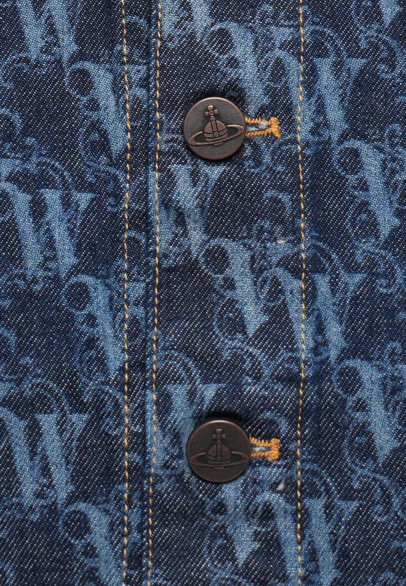 Tessuto denim con un motivo a monogramma tonale blu. Due bottoni scuri con un logo e cuciture gialle visibili lungo la cucitura.