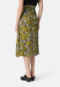 Groene bloemen midi rok met zwart-witte patronen, zachte textuur, aansluitende taille en A-lijn vorm, gecombineerd met zwarte hoge mules.