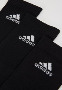Mustadest puuvillast sokid, millel on ribakujundus ja valge Adidas'i logo. Näidatud on kolm paari, millel on logo sokiküljel.