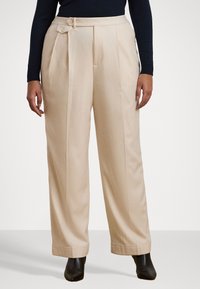 Pantaloni beige a vita alta con pince, bottone laterale e gamba dritta. Tessuto morbido e orli larghi. Indossati con stivali alla caviglia.