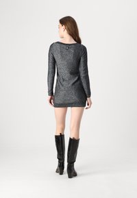 Long-sleeve, fitted dress in black with silver shimmer; features a boat neckline, ribbed hem, and worn with black knee-high boots.