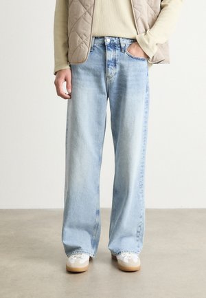 Hellblaue Denim-Breitbeinform-Jeans mit einem ausgewaschenen Look, subtilen Wischspuren und einem Fünf-Taschen-Design, kombiniert mit weißen Sneakern auf einer glatten Oberfläche.