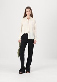 Light cream button-up shirt with ruffled collar and textured detailing, paired with black pants featuring side stripes and open-flare hems.