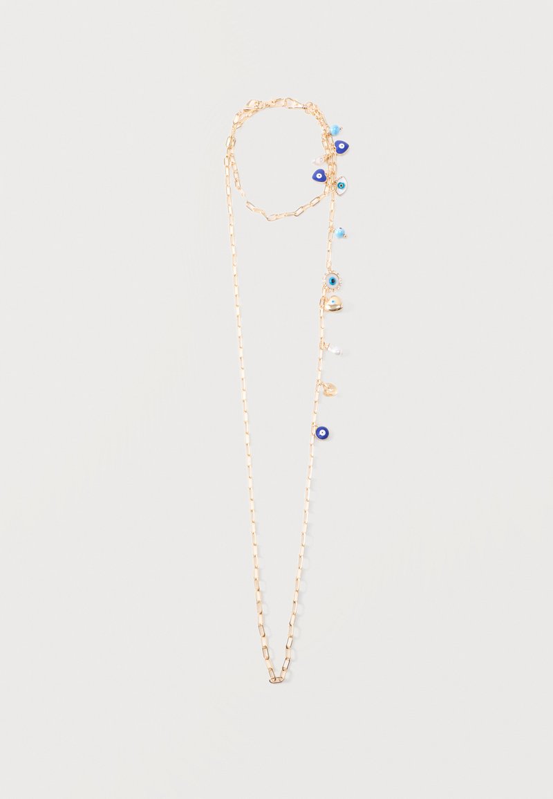 Kuldne kett-kaelakee sinise kuri silma, pärli ja kuldsete võluhelmeste reas, mis asetsevad ühelt poolt tavalise tausta ees.