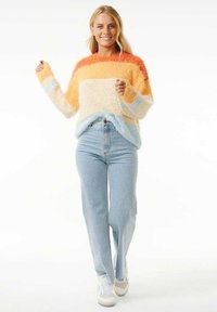 Suéter colorido y suave en franjas naranjas, amarillas y azul claro, con un corte relajado y aberturas laterales, combinado con unos jeans de talle alto en azul claro.