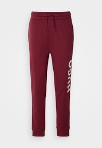 Bordeauxfarbene Sweatpants aus weichem Stoff, mit elastischem Bund, Kordelzug und großem weißen "HUGO" Logo am linken Bein.