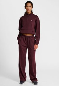 Bordeaux cropped sweatshirt met hoge kraag en roze logo, gecombineerd met bijpassende losse sweatpants met zijzakken en elastische tailleband.
