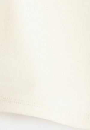 Posnetek v bližini krémasto obarvanega blaga, ki prikazuje fino pleteno teksturo in šivano robno obdelavo na spodnjem robu.